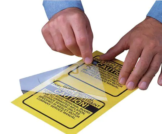 Hands applying 3M Polyester Gloss Overlaminate over yellow caution warning label.