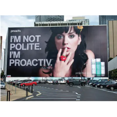 Large parking lot billboard displaying a woman advertising Proactiv skin care products. Caption reads
