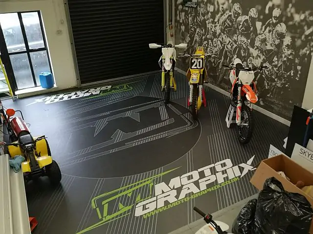 Three dirt bikes displayed in a sporting goods store on grey floor with green and white Moto Graphix logo.