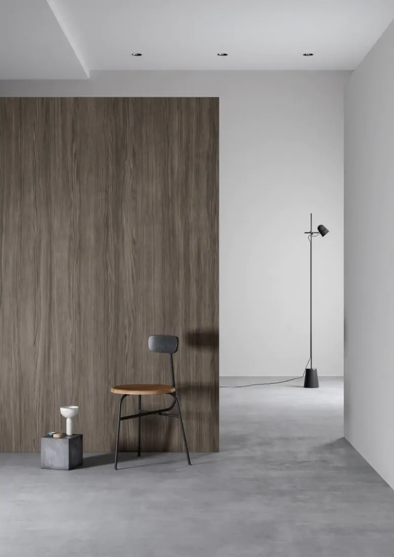 A chair in front of a large panel with a grey wooden vinyl finish. Light on thin stand in the background.