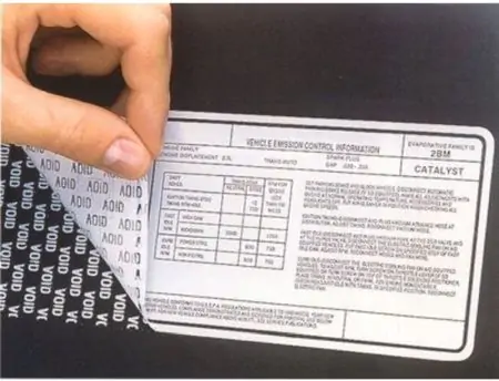 Hand applying Vehicle Emission Control Information label to black surface using 3M 7381 Tamper Evident Label Material.