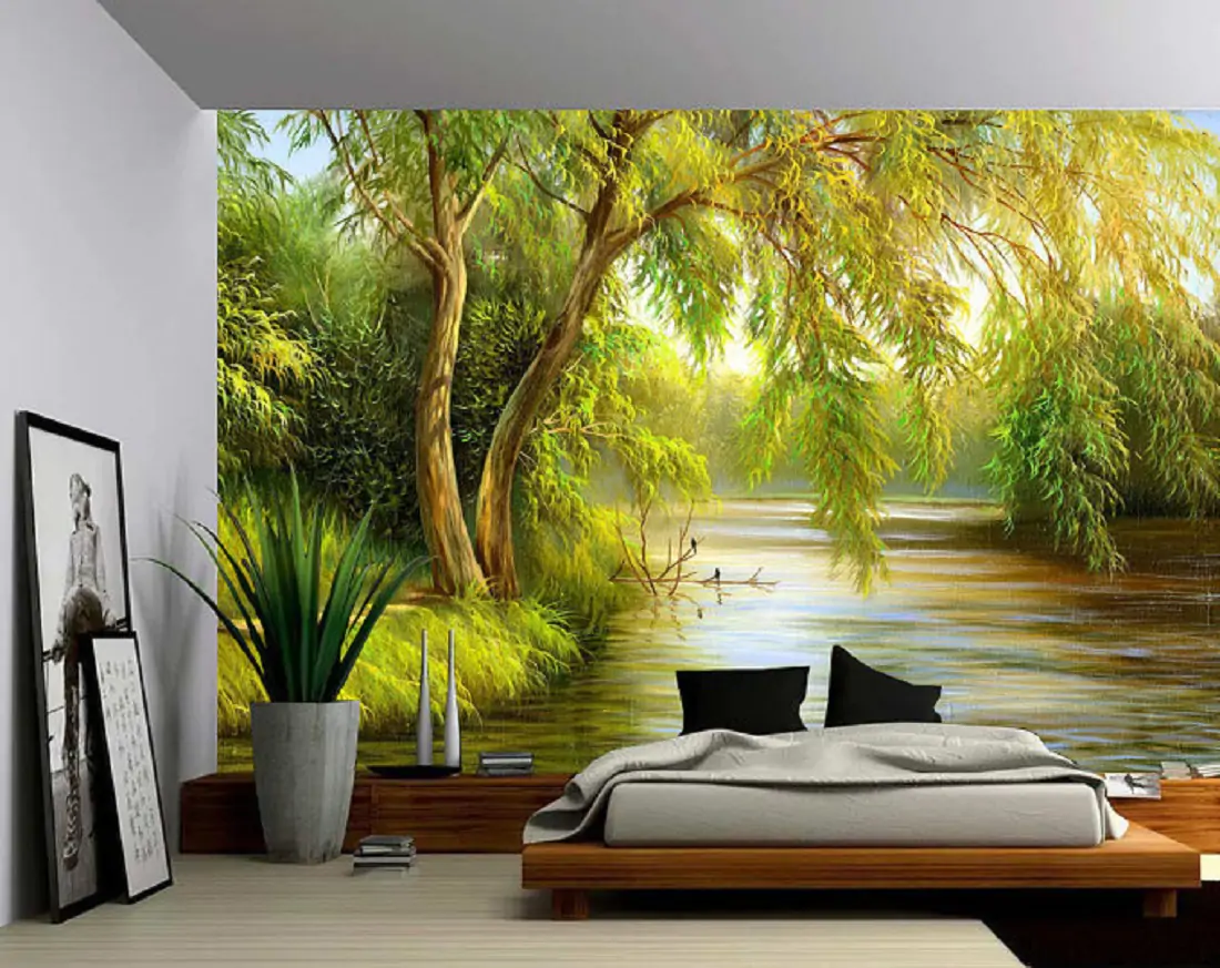 A room with a bed and on the wall is a mural of a river and green trees 