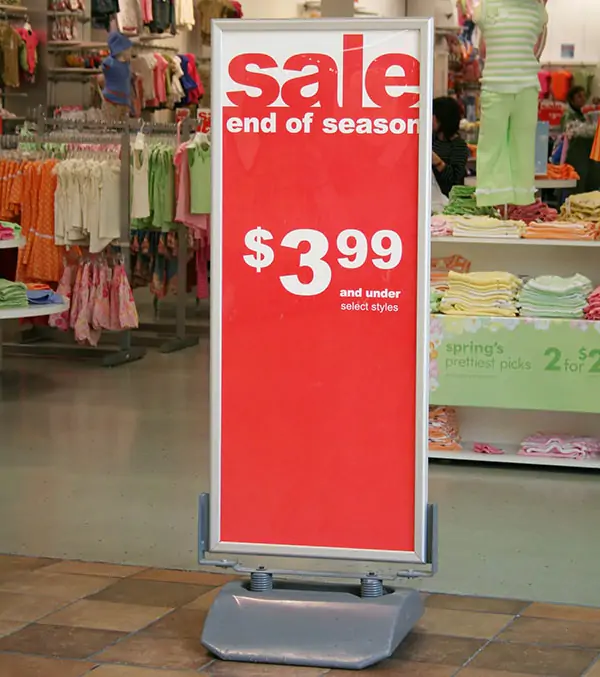 A clothing store in the background and a poster stand that tells the sale in red 