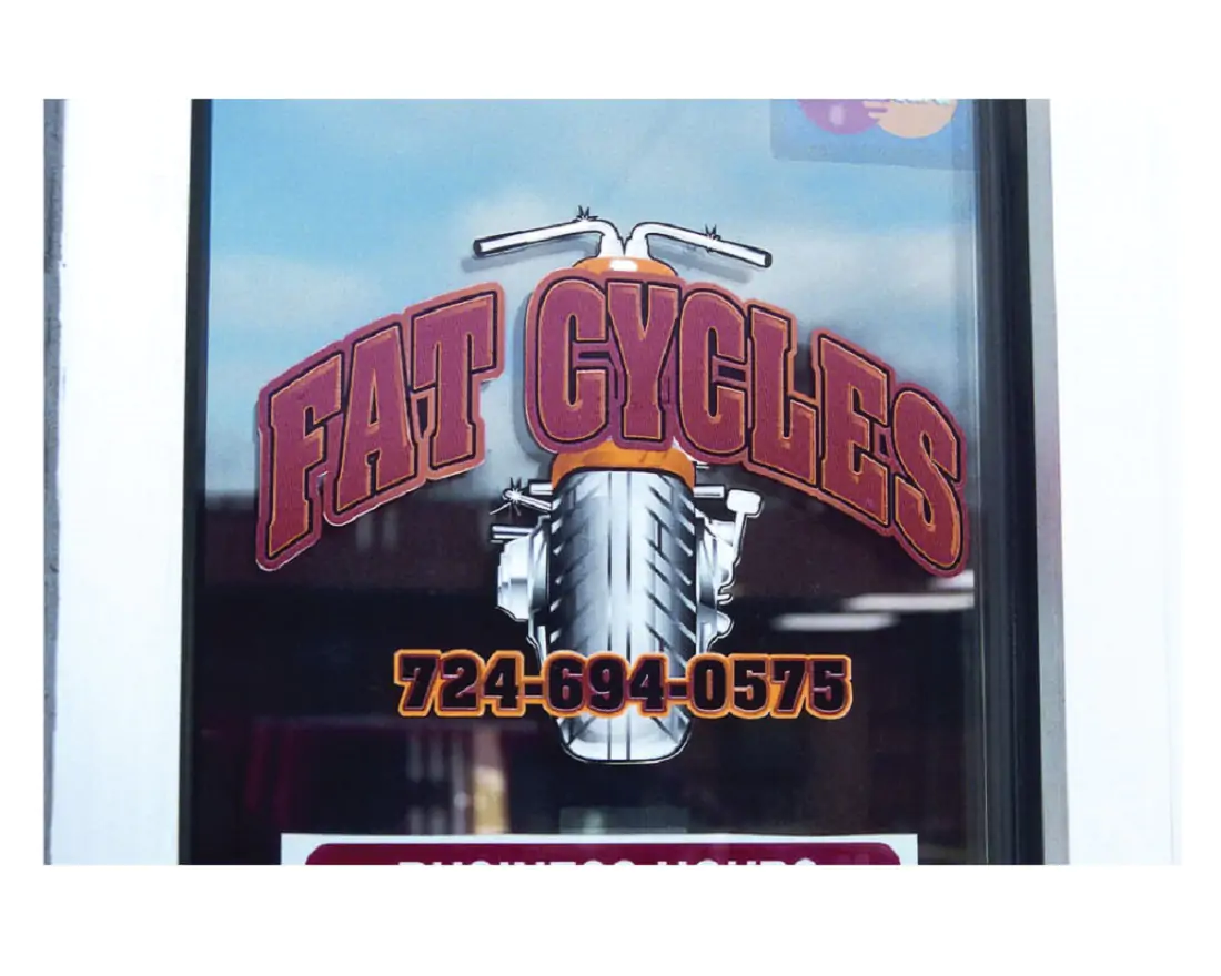 A sign on a window that is red and orange for Fat Cycles 