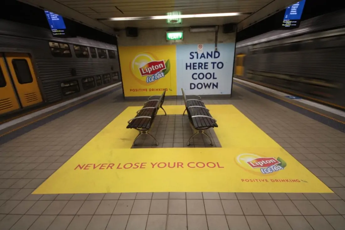 A subway station, with yellow square painted around the benches and a yellow and blue Lipton advertisement on the walls 