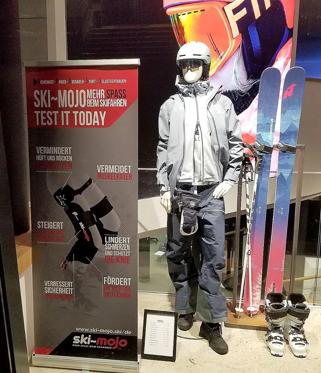 Banner on a stand with ski supply info, a manikin in a ski outfit standing next to the sign and skis